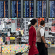 Flight attendants walk past an electric display board covered with notes and posters at Hong Kong’s airport on Aug. 13, 2019, the day after the airport closed due to protests.